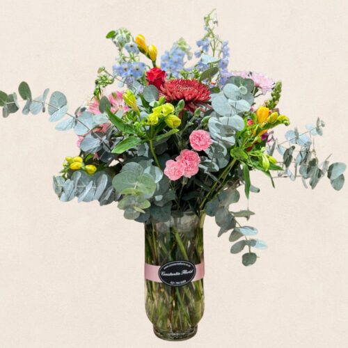 Lantern Vase Arrangement with seasonal flowers displayed in a tall glass vase that narrows at the base and flares at the top, available in various sizes and colours.