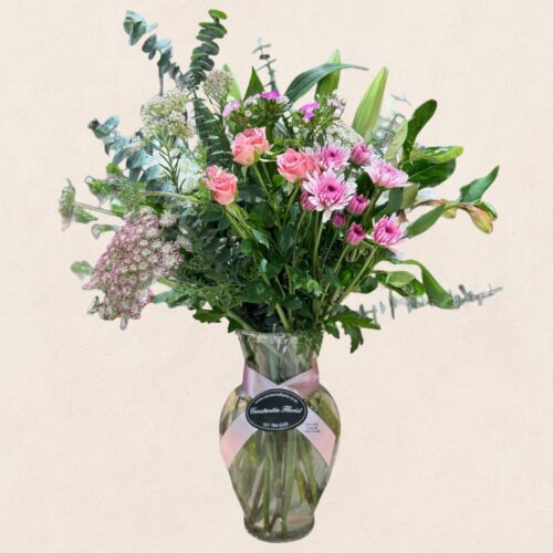 Spring Valley Vase with seasonal flower arrangement displayed in a curved glass vase with a flared top, featuring assorted blooms in various colours.